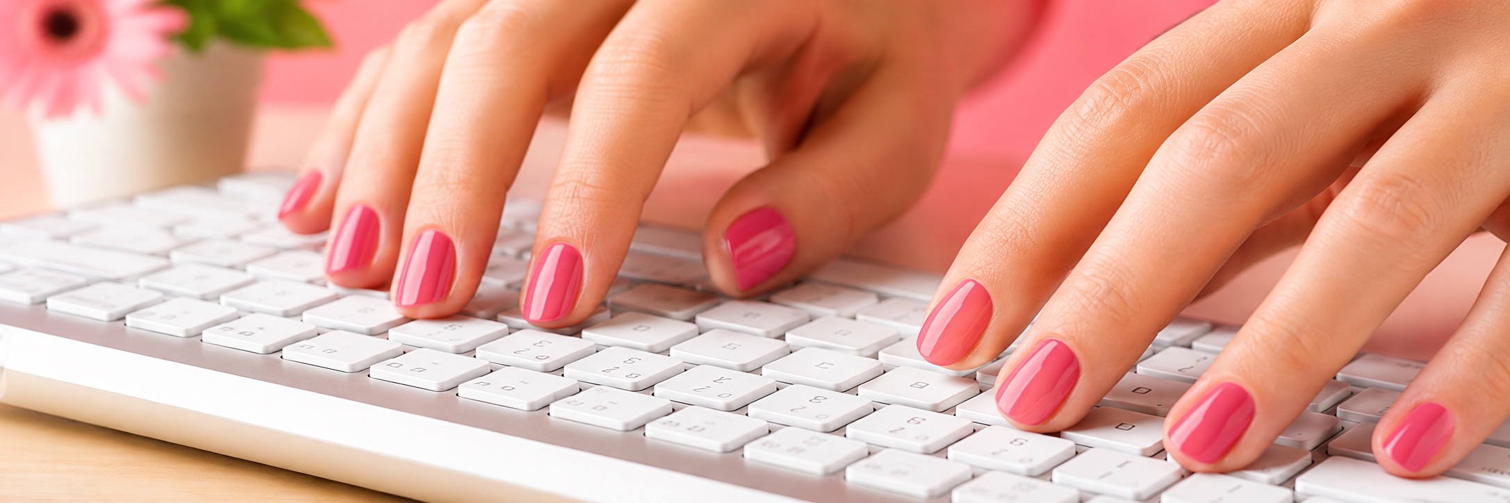 Hands with pink nail polish typing on a white keyboard