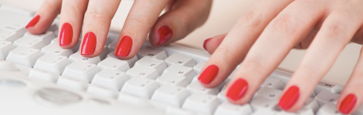 Hands with red nail polish typing on a white keyboard